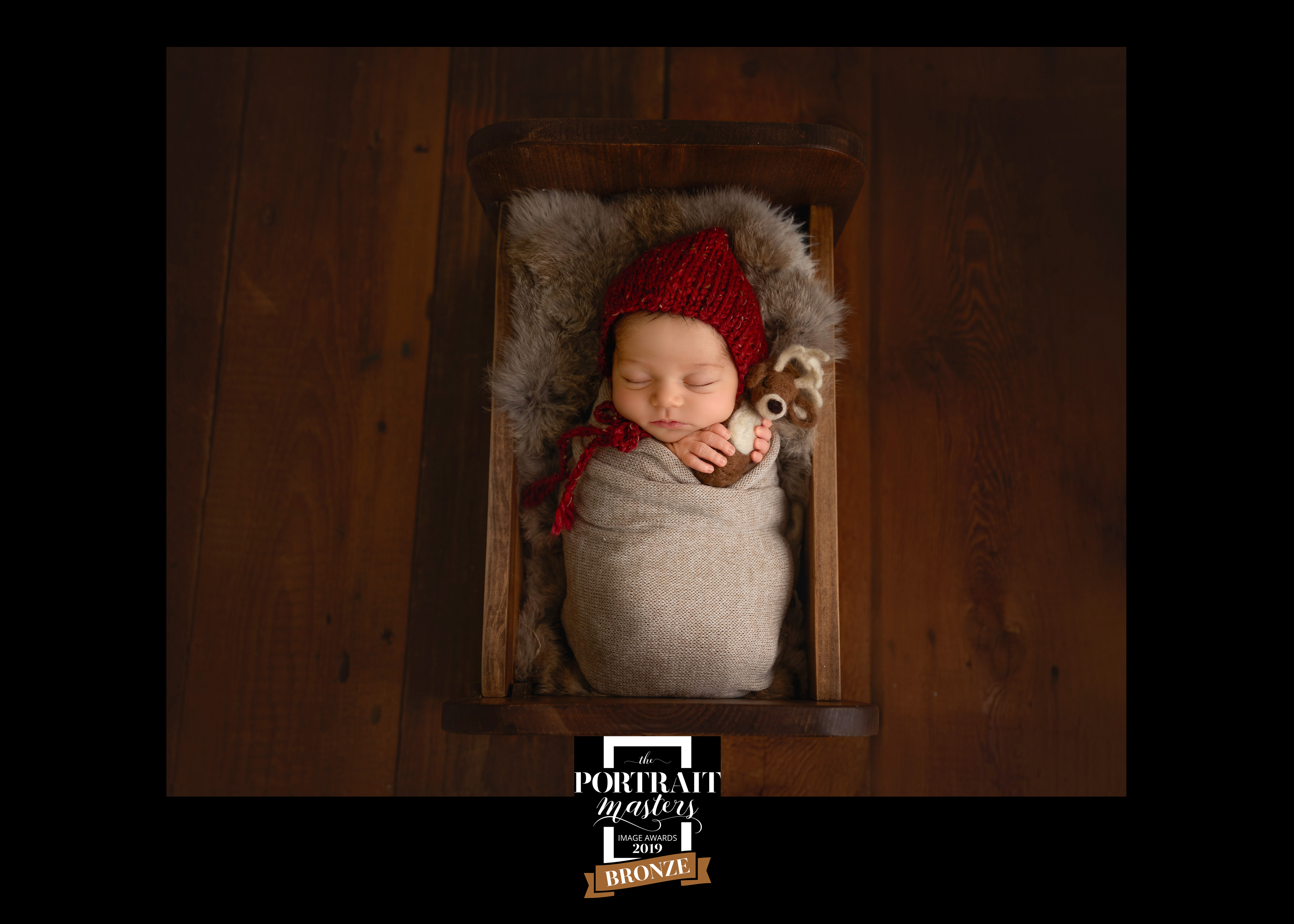 newborn red bonnet holding reindeer toy animal fur wood bed
