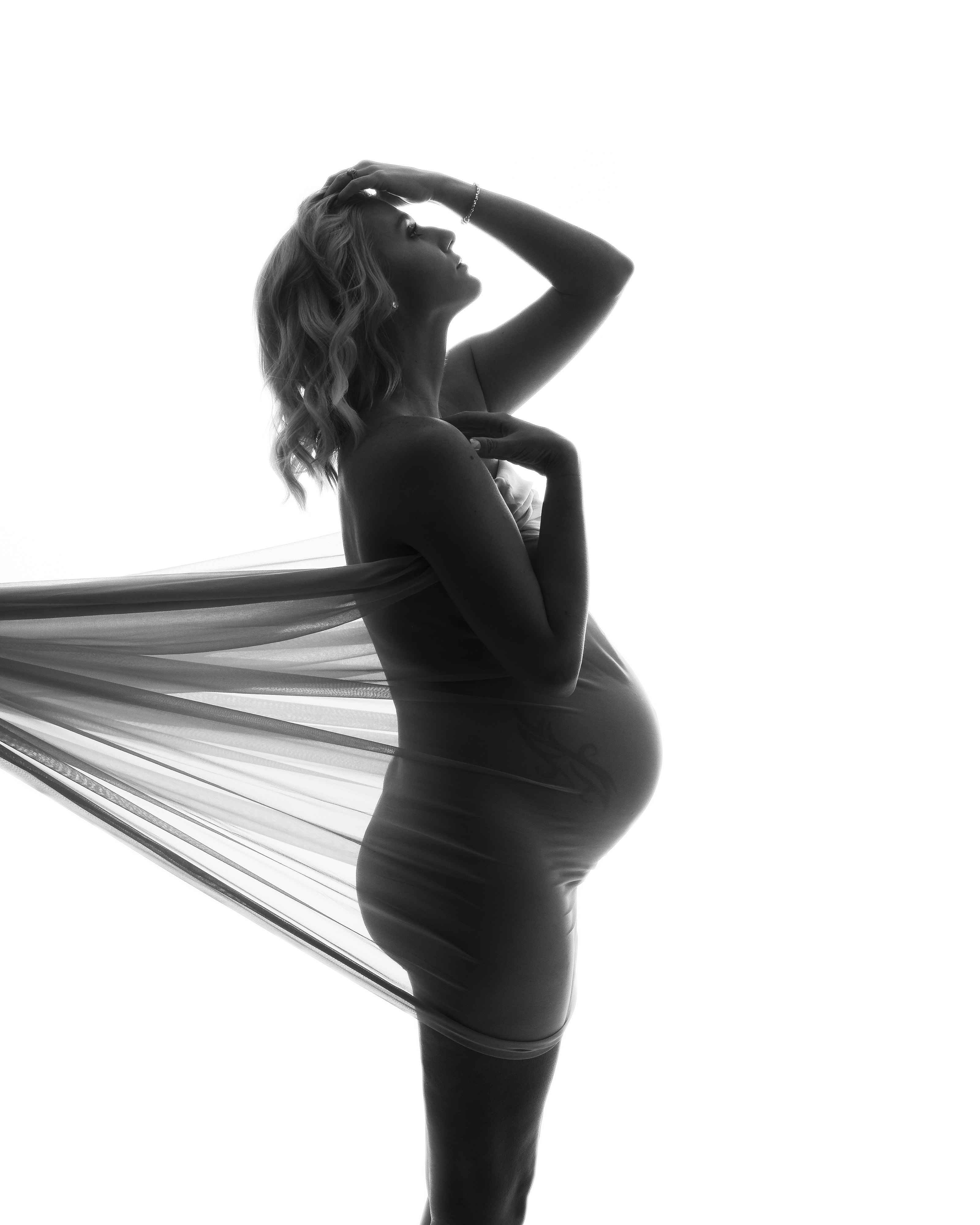 Maternity Photography, a black and white image of a pregnant mother in a studio with tule wrapped around her, a tattoo peaks through the tule