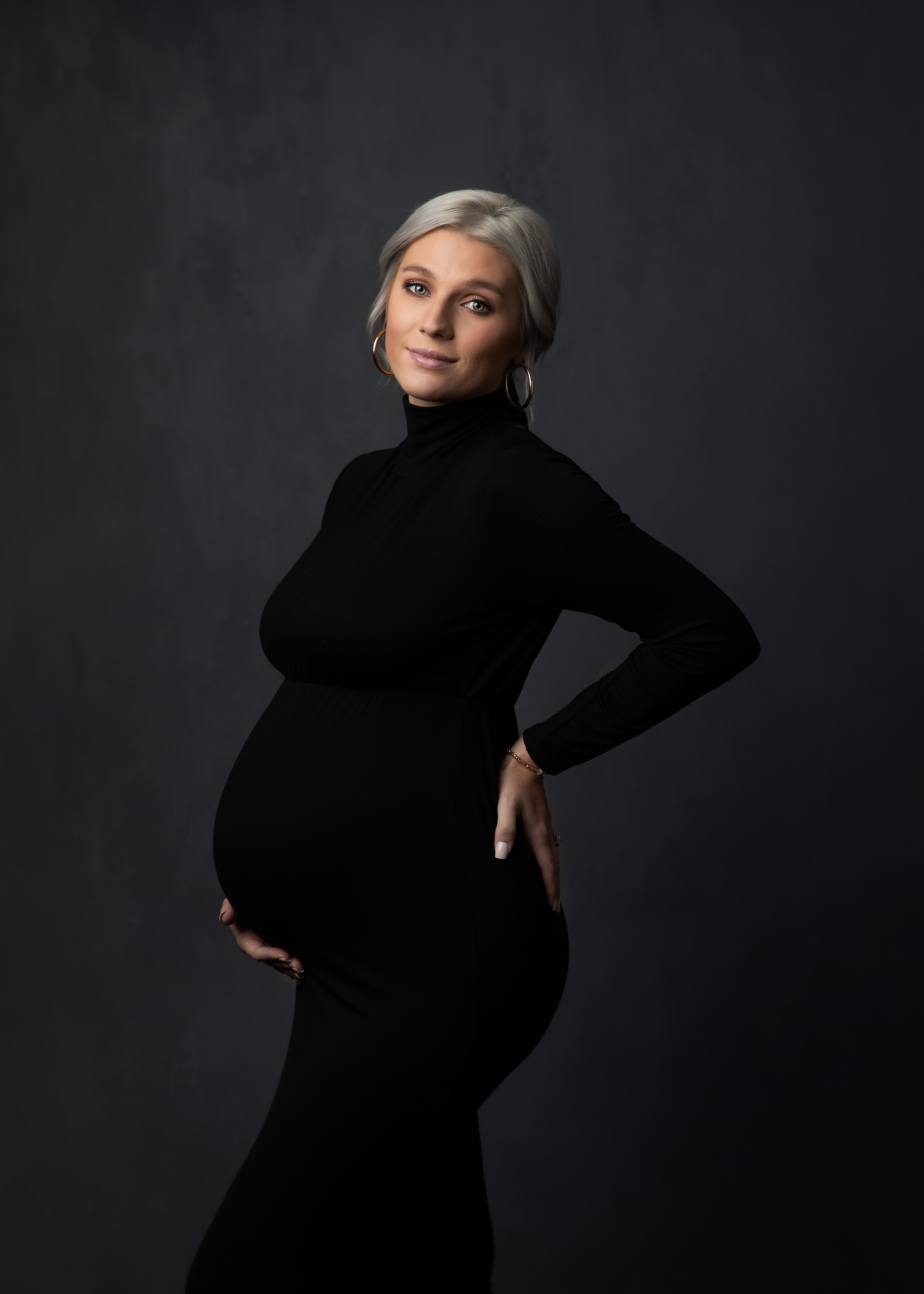 Maternity Photographer, an expectant mother wears a black skirt and holds her belly happily in the studio