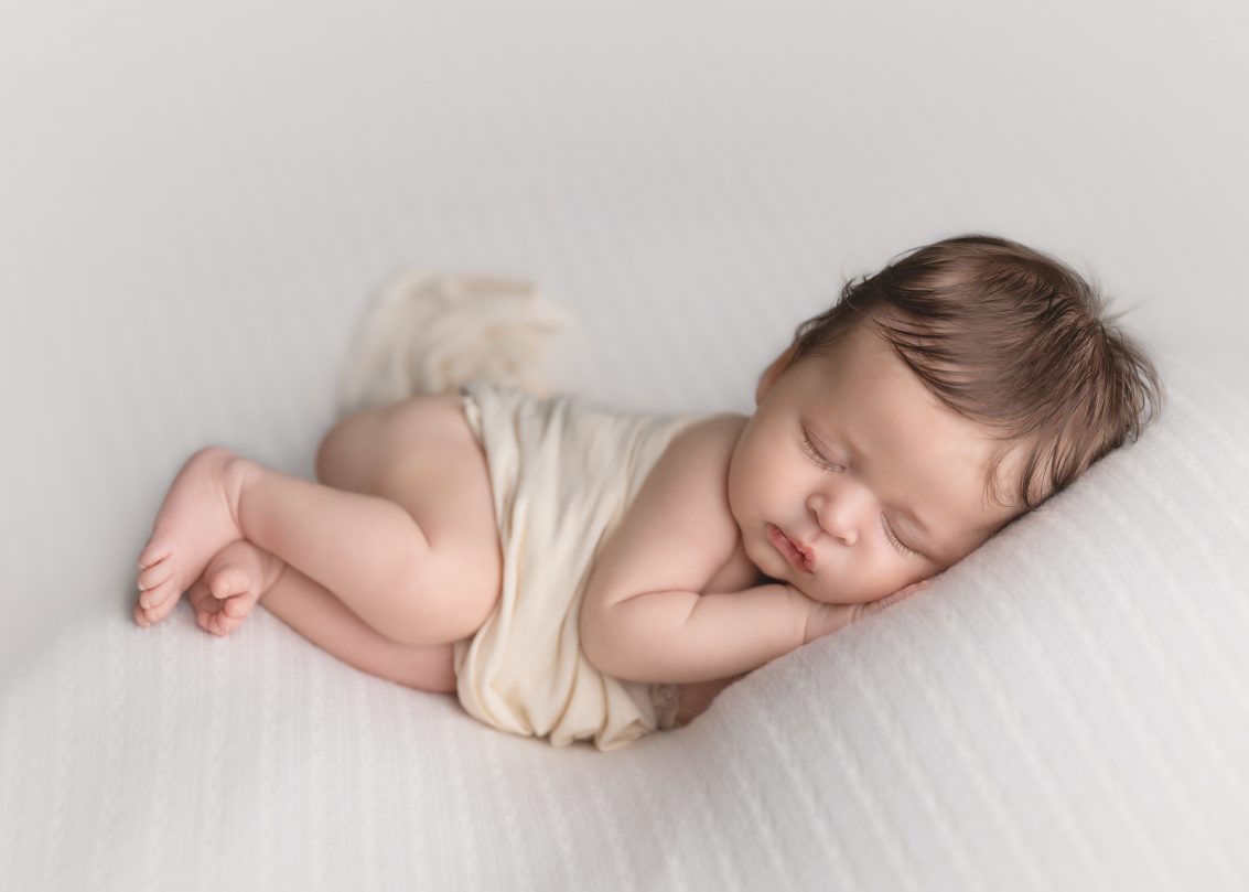 Newborn Photographer, a baby lays cuddled in blankets on a pillow